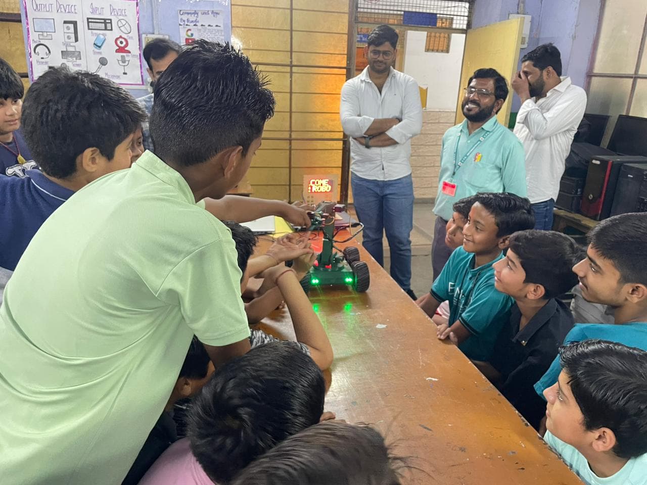 A student steers a small robot car across the table while classmates lean in to watch