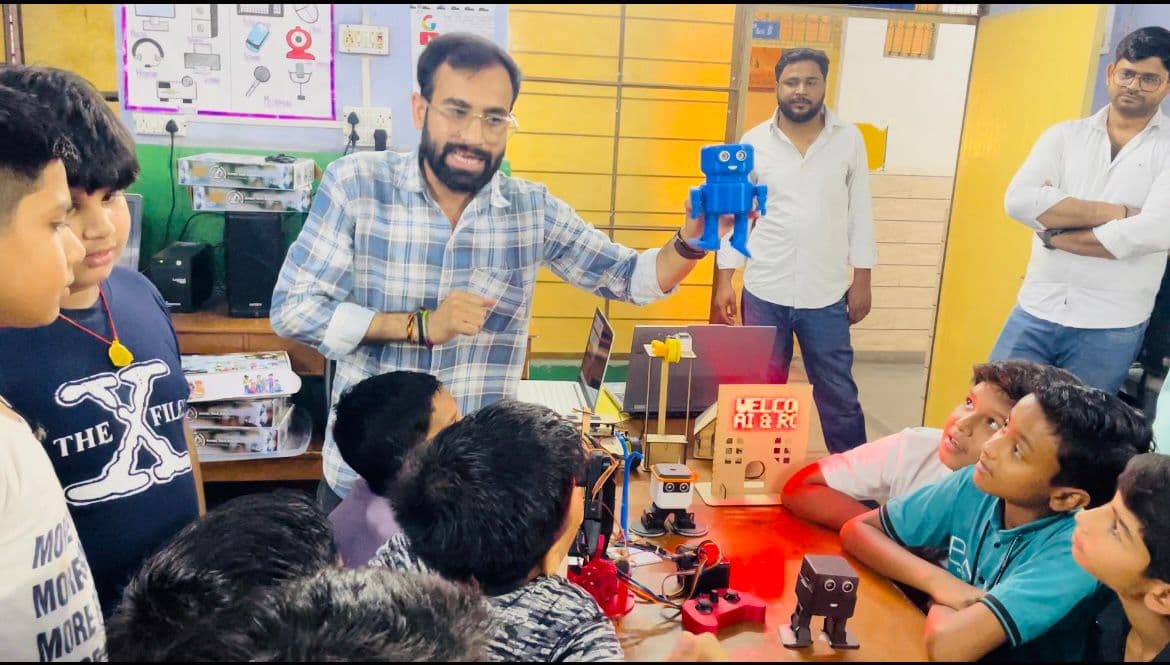 A mentor demonstrates a small blue robot to students